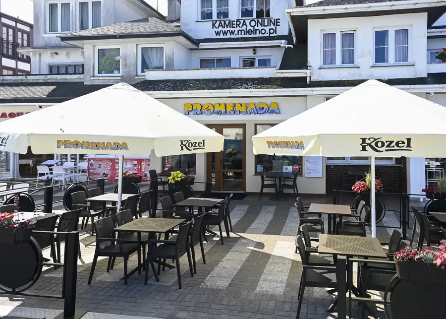 Ogródek z parasolami przed budynkiem z szyldem Promenada